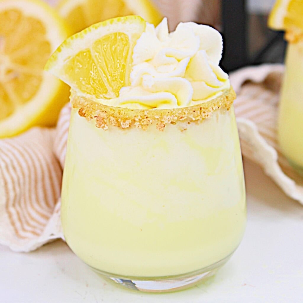 Yellow lemon dessert drink with whipped cream and lemon slice in a glass.