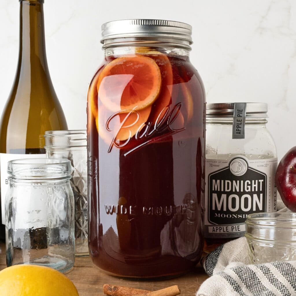 Large mason jar with sangria, citrus slices, surrounded by jars and a lemon.