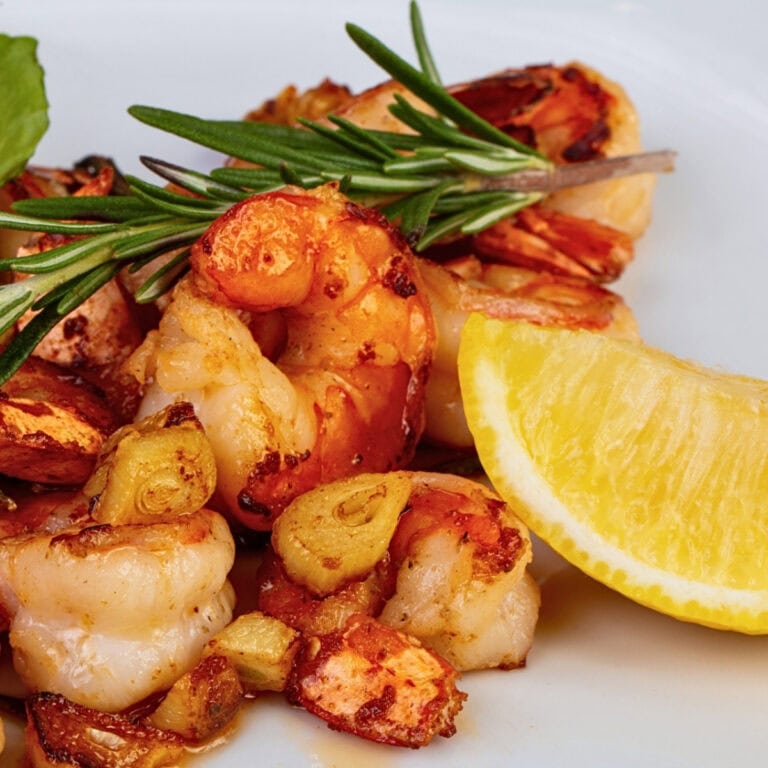 Grilled shrimp with garlic, rosemary, and a lemon wedge on a white plate.