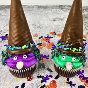 Two cupcakes decorated as witches with hats, faces, and colorful frosting.
