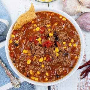 Bowl of chili with corn, ground beef, tortilla chip, and visible seasonings.