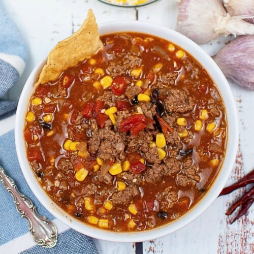 Bowl of chili with corn, ground beef, tortilla chip, and visible seasonings.