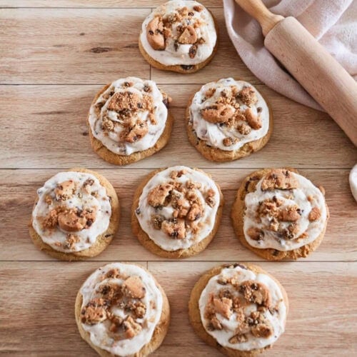 Eight frosted cookies topped with crumbled cookies on a wooden surface.