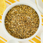 Bowl of lemon pepper seasoning on a yellow and white striped cloth.