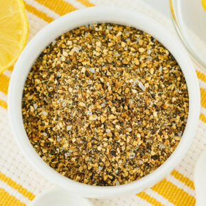 Bowl of lemon pepper seasoning on a yellow and white striped cloth.