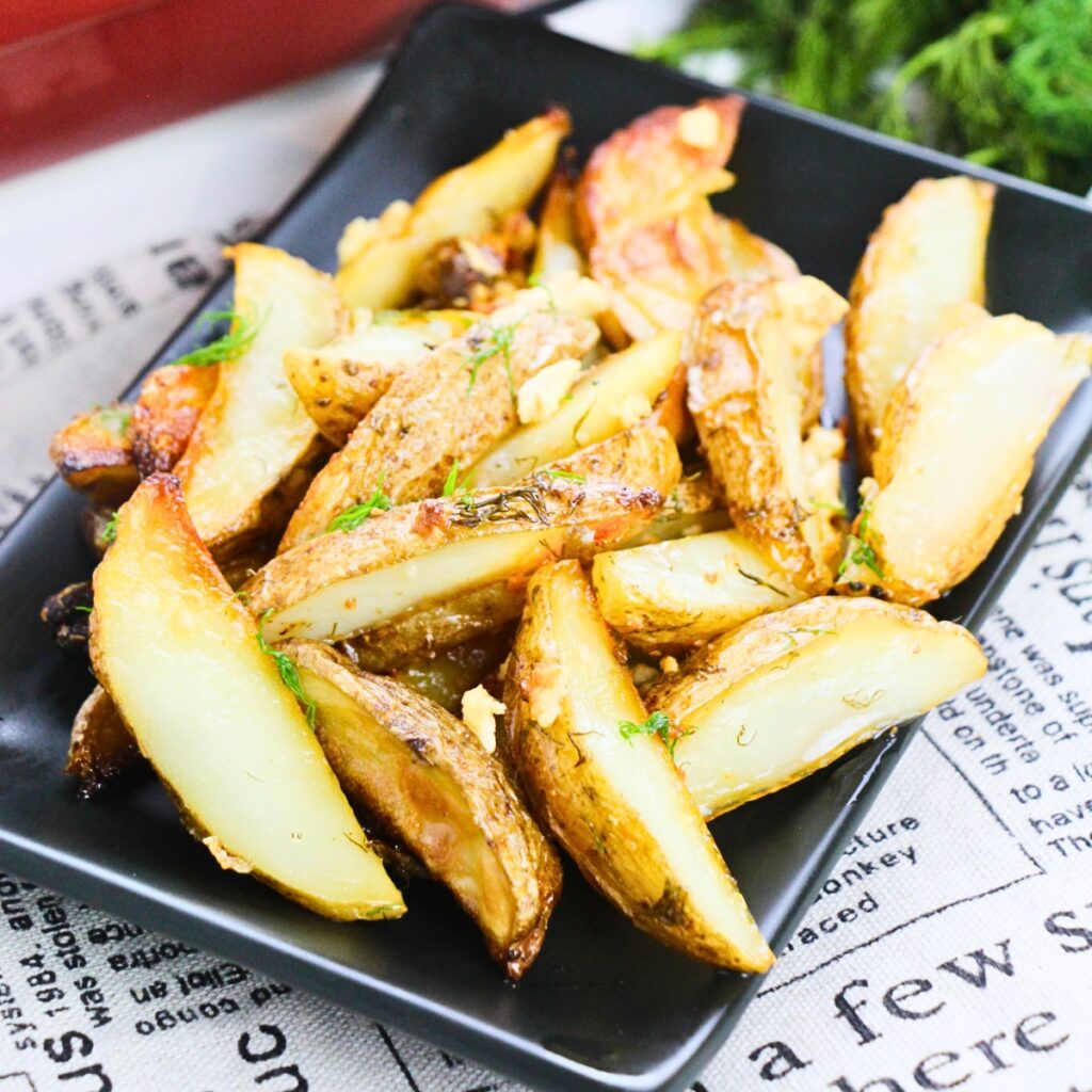 Golden potato wedges garnished with herbs on a black rectangular plate.