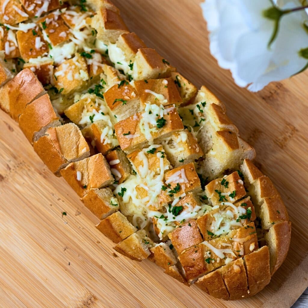 Sliced cheesy garlic bread with herbs on a wooden board.