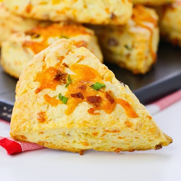 A cheddar scone topped with melted cheese and chives on a white table.