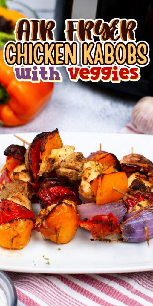 Chicken kabobs with peppers and onions on a white plate near fresh veggies.