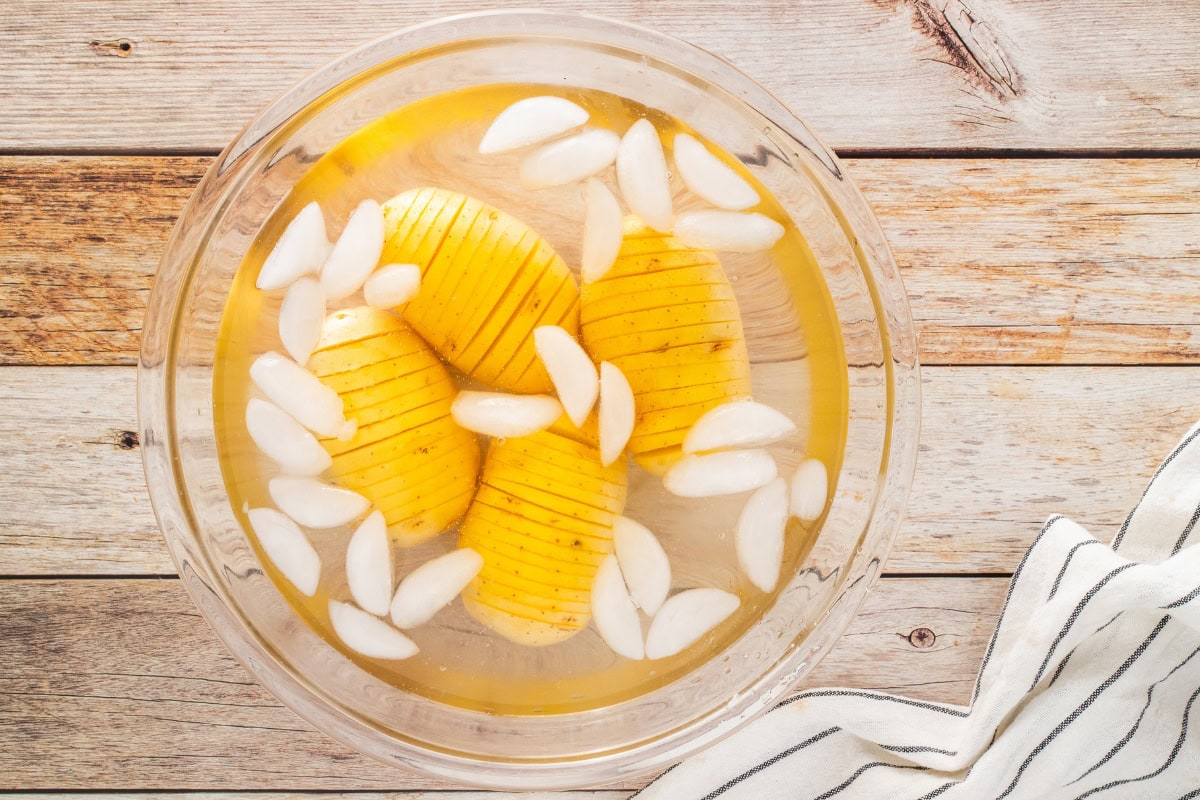 Sliced potatoes soaking in ice water in a glass bowl on a wooden surface.