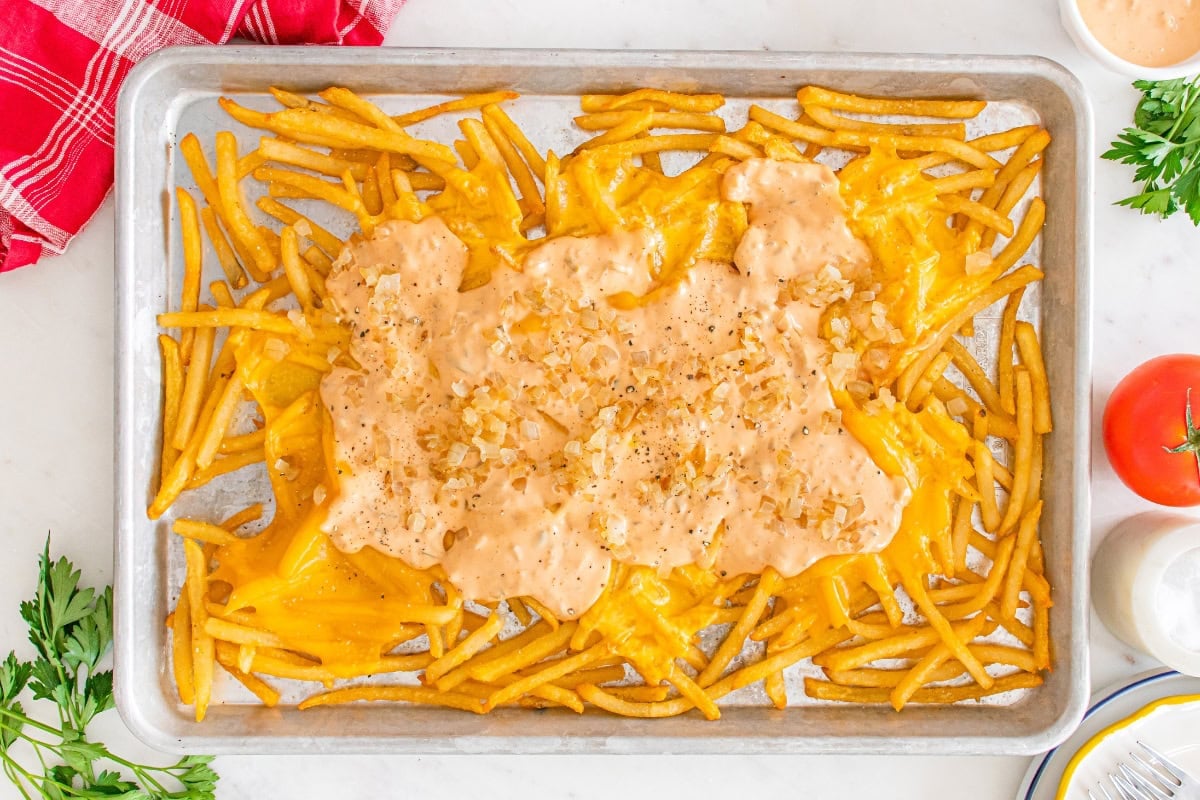 Fries topped with melted cheese and sauce on a baking sheet.