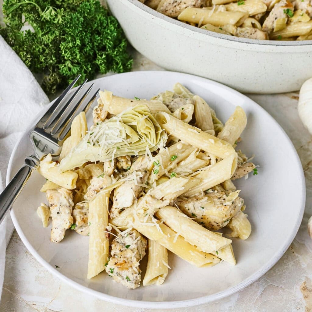 A plate of creamy penne pasta with chicken, artichokes, and grated cheese.