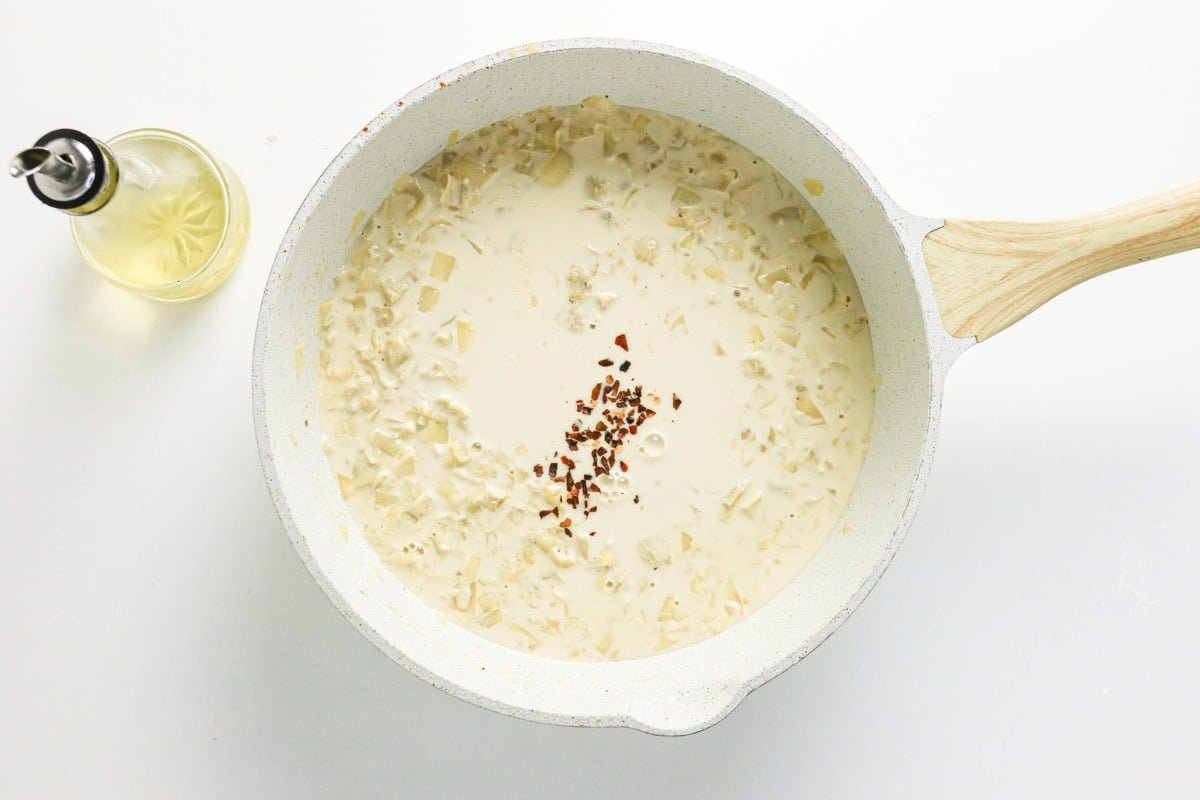 Creamy sauce with onions and chili flakes in a white pan, oil bottle beside it.