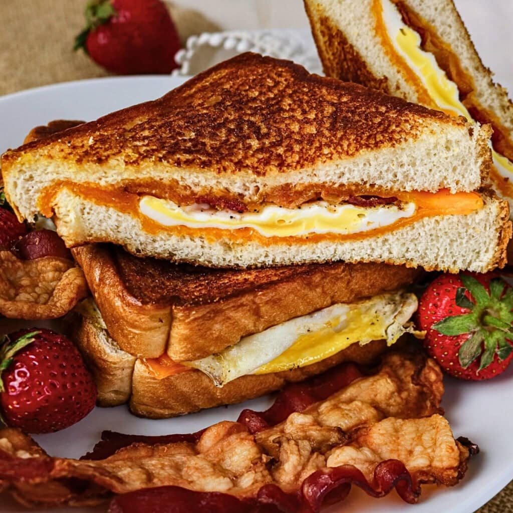 Grilled cheese sandwiches with egg, bacon, and strawberries on a plate.