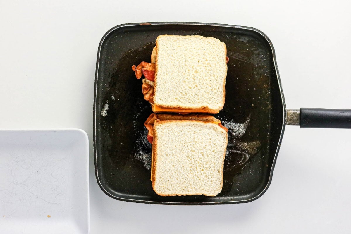 Two sandwiches cooking in a black pan on a white background.