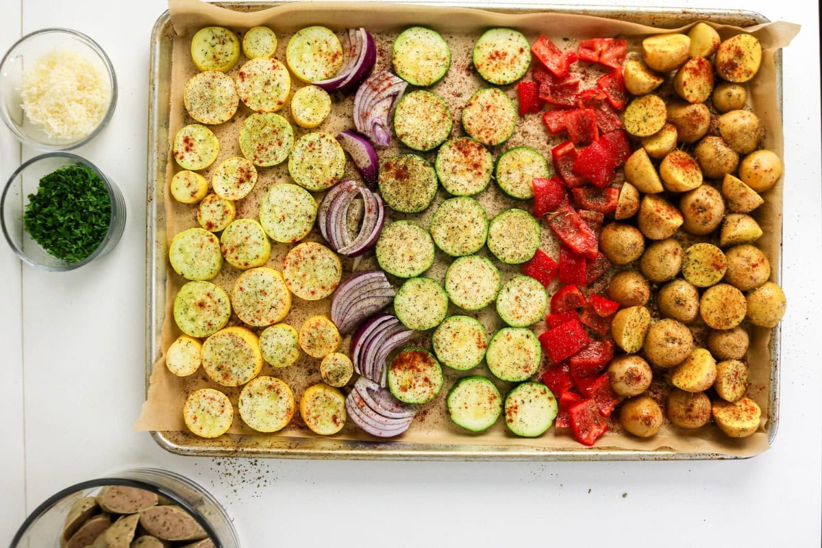 Sliced veggies on a baking sheet, ready for roasting, with seasonings nearby.