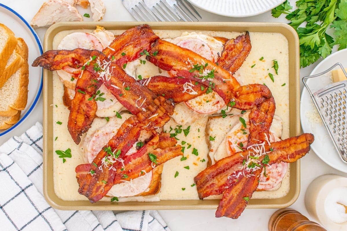 Bacon tops toast, turkey, tomato, and cheese, garnished with herbs and parmesan.