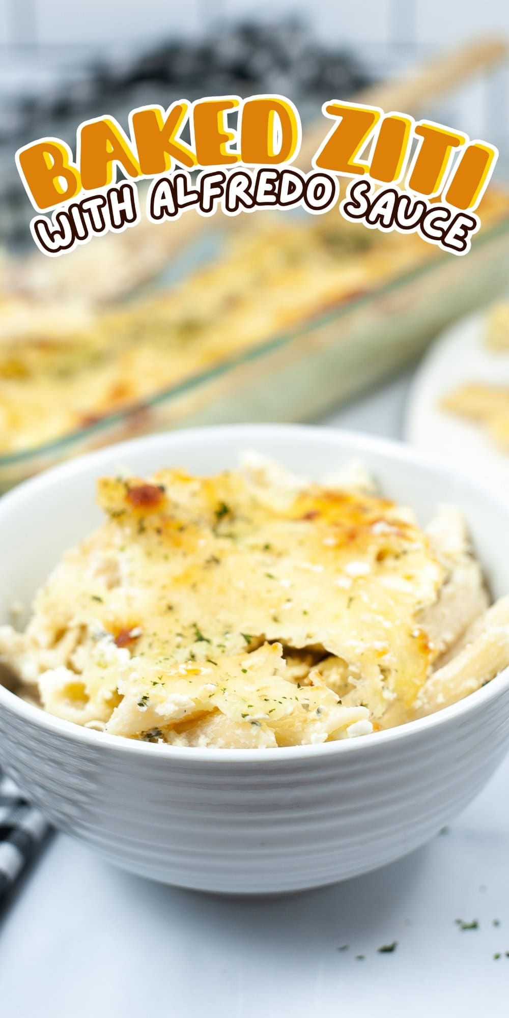 Bowl of baked ziti with Alfredo sauce, casserole dish in background.