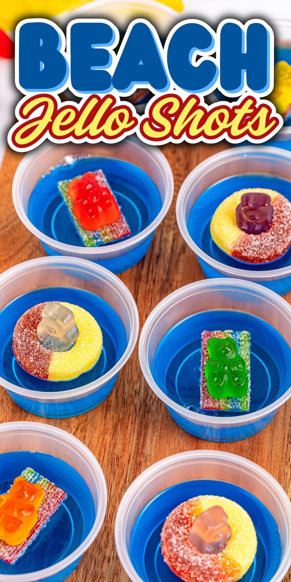 Six blue jello shots with candy decorations on a wooden surface.