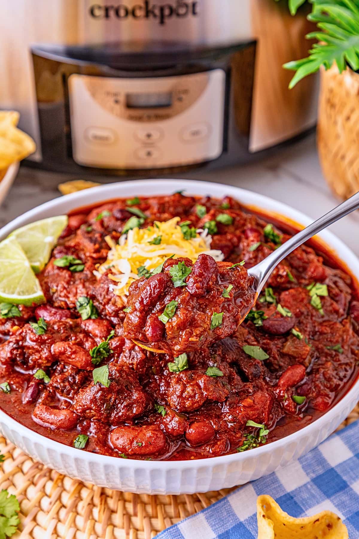 Bowl of chili with beans, cheese, and herbs, with a spoon and lime wedges.