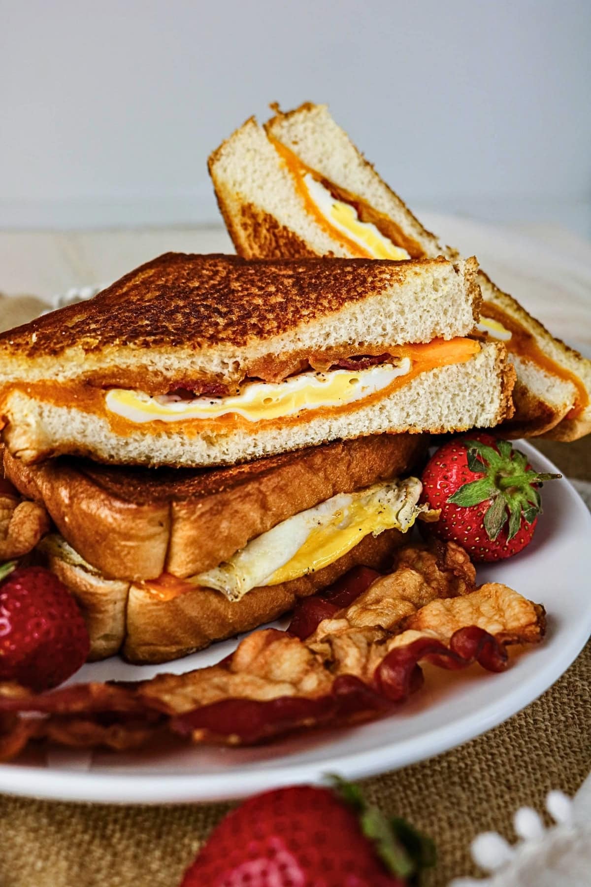Stacked grilled cheese sandwiches with egg, bacon, and strawberries on a plate.