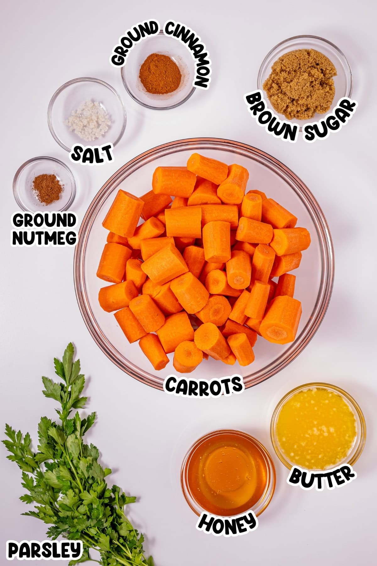 Bowl of carrots with spices, brown sugar, honey, butter, and parsley around it.