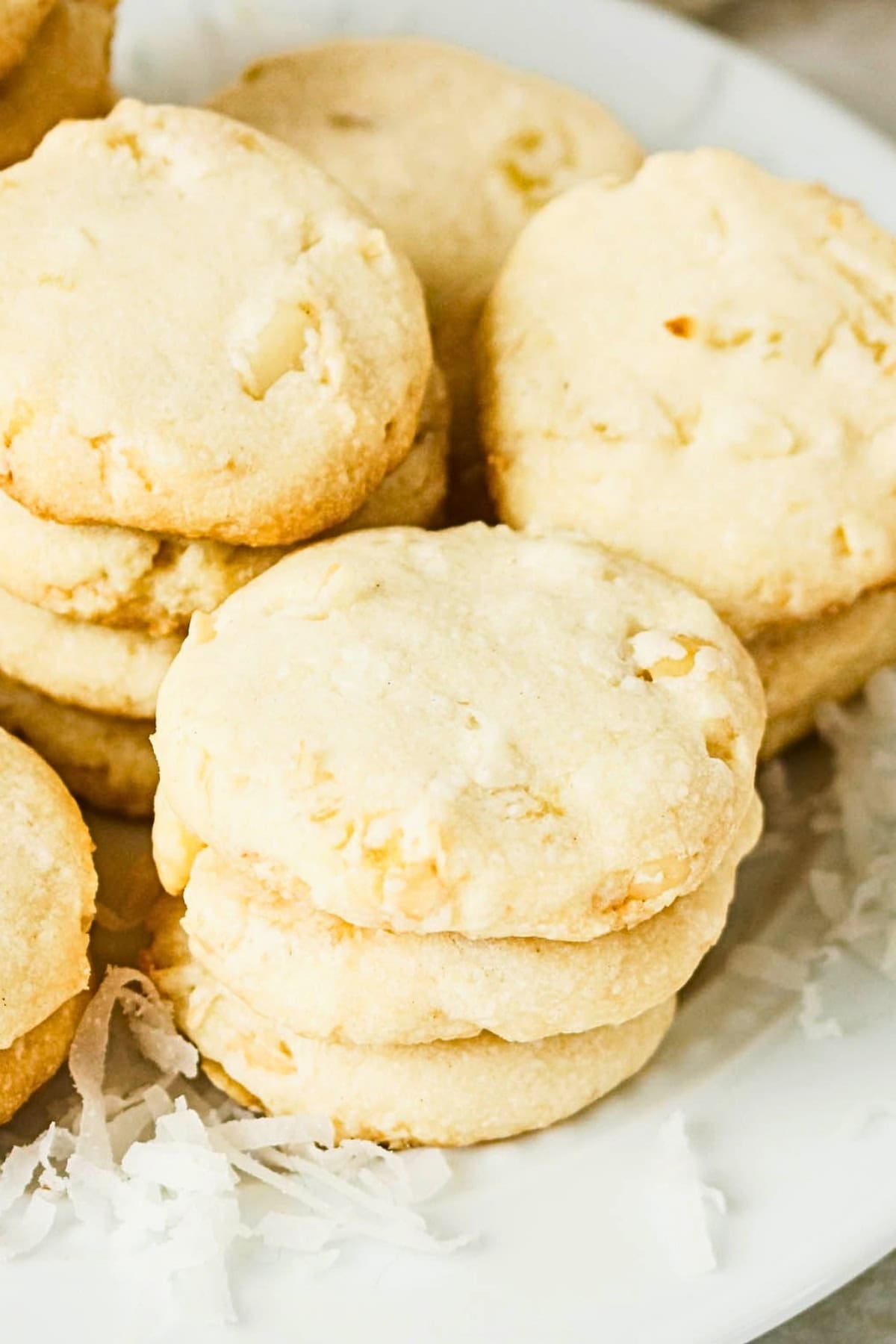 Stacks of coconut cookies on a white plate with shredded coconut nearby.