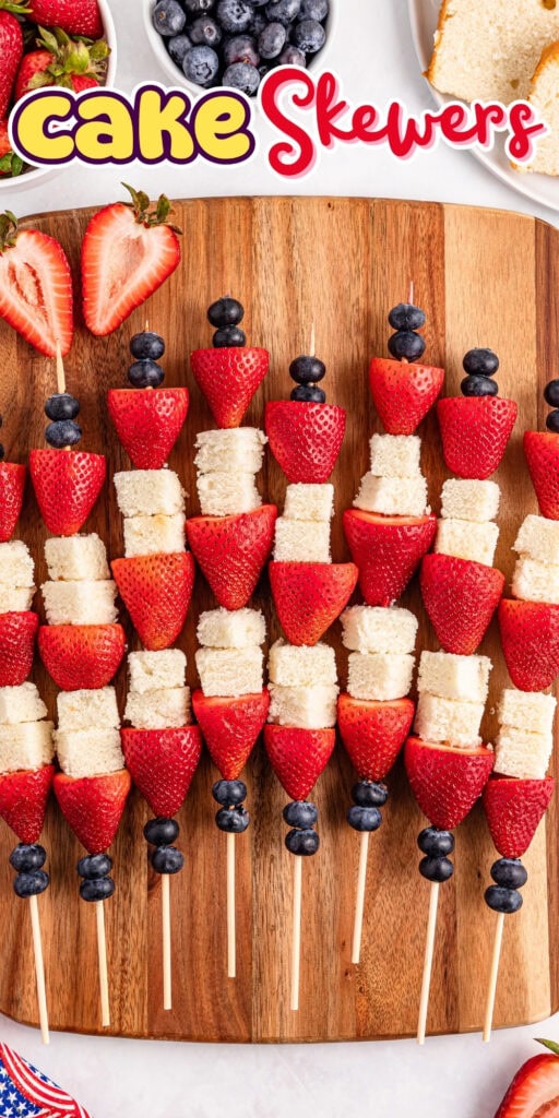 Wooden skewers with strawberries, blueberries, and cake cubes on a board.