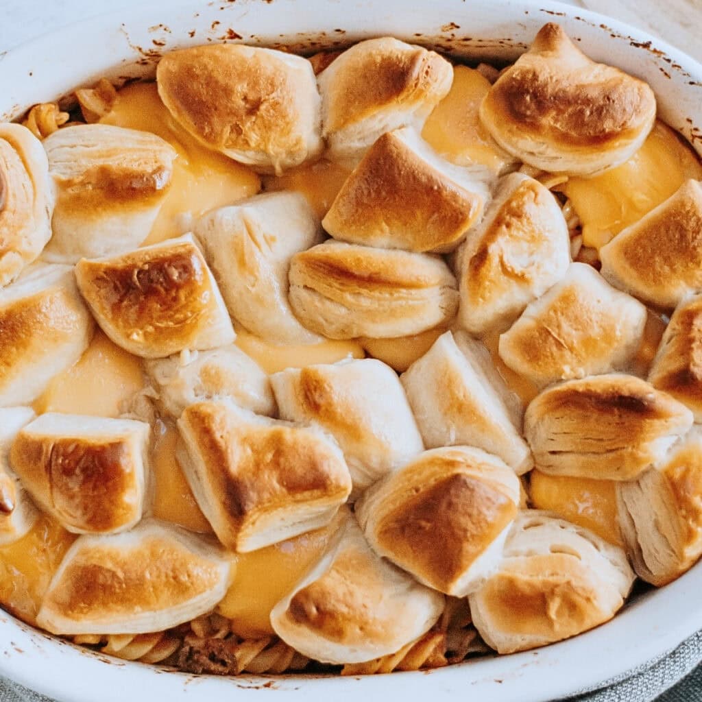 Golden biscuit pieces on top of a cheesy baked casserole in a white dish.