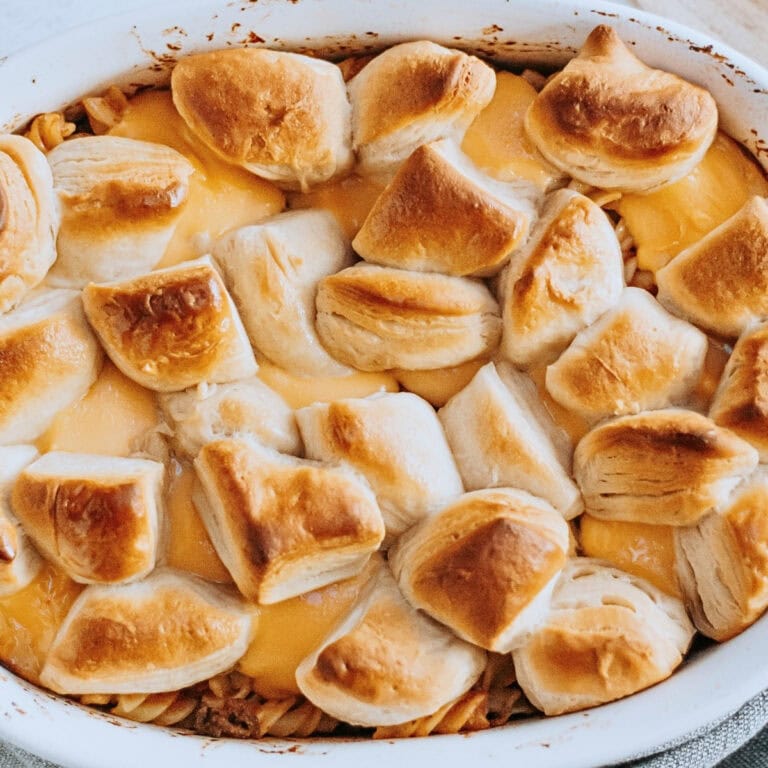 Golden biscuit pieces on top of a cheesy baked casserole in a white dish.
