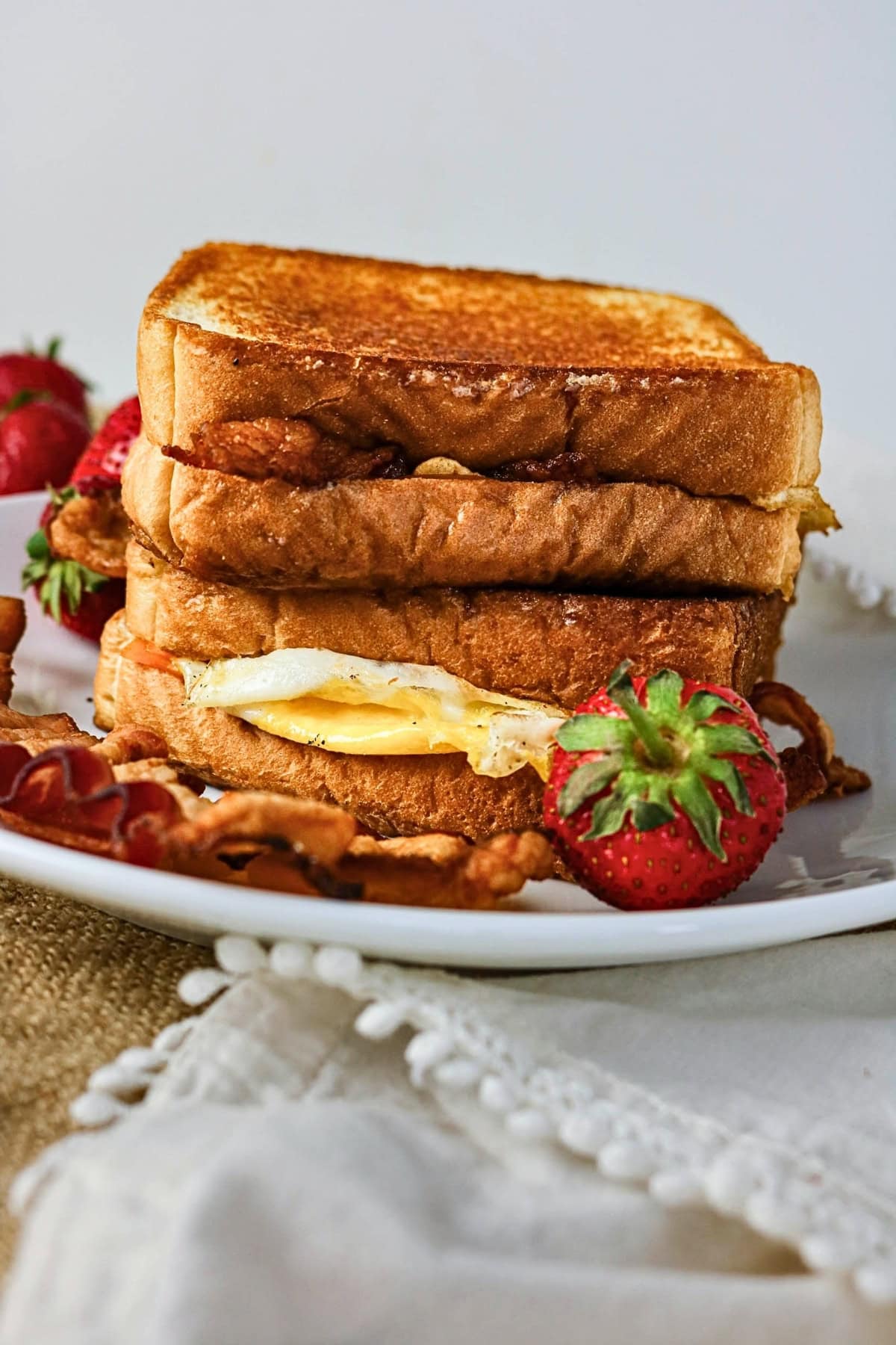 Stacked breakfast sandwiches with egg and bacon, served with strawberries.