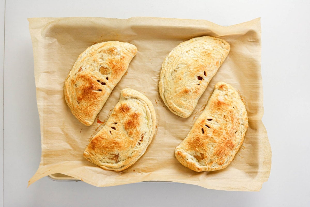 Four golden-brown hand pies on parchment paper in a baking tray.