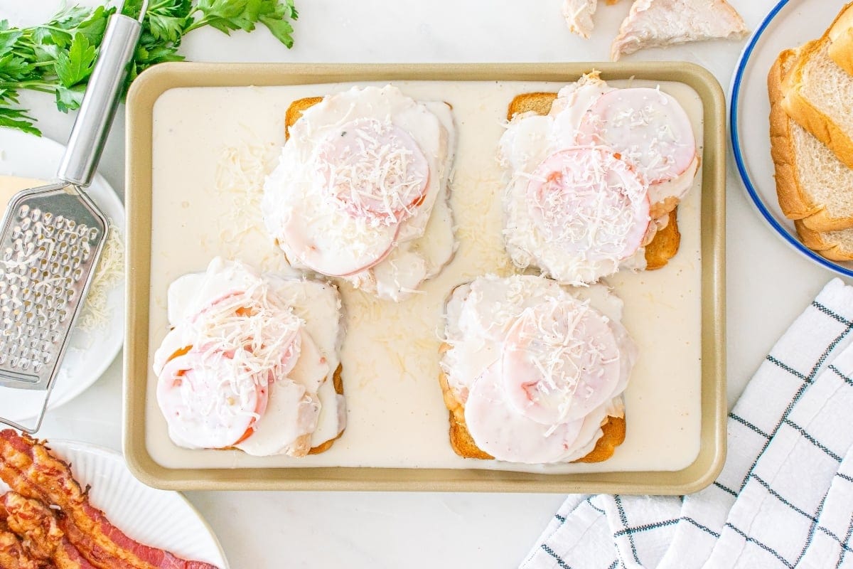 Four open-faced sandwiches with tomatoes and cheese on a baking sheet.