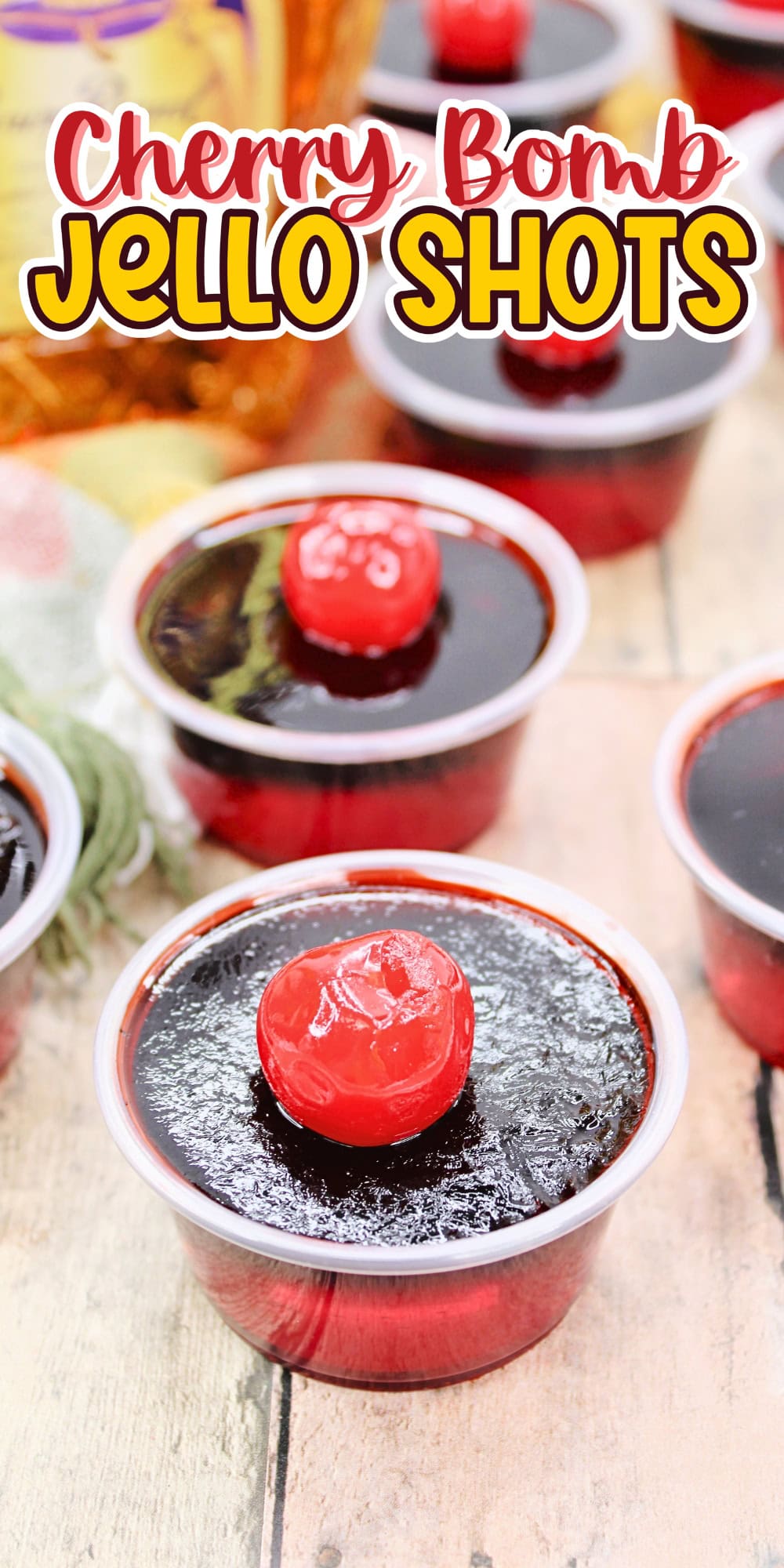 Cherry-topped jello shots in small cups on a wooden surface.