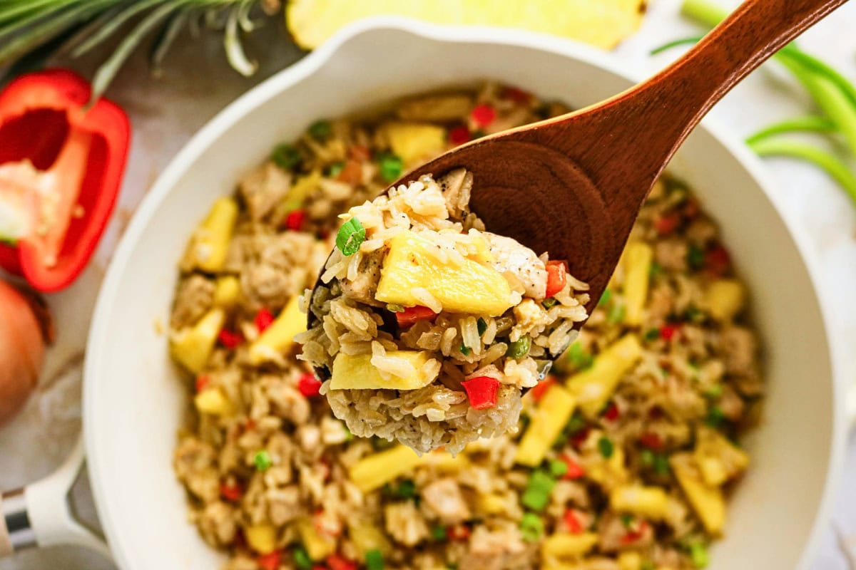 Spoon holding pineapple fried rice over a bowl filled with the same dish.