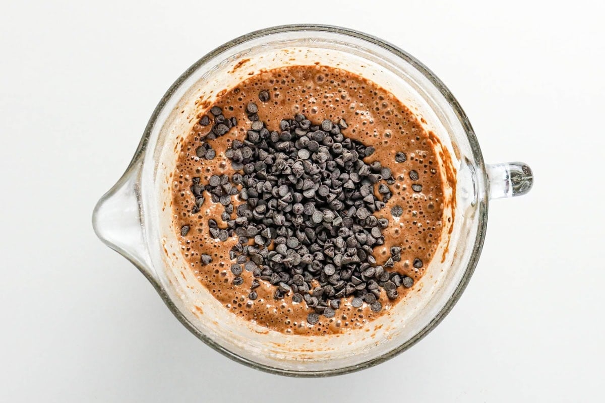 A mixing bowl contains chocolate batter topped with a layer of chocolate chips.