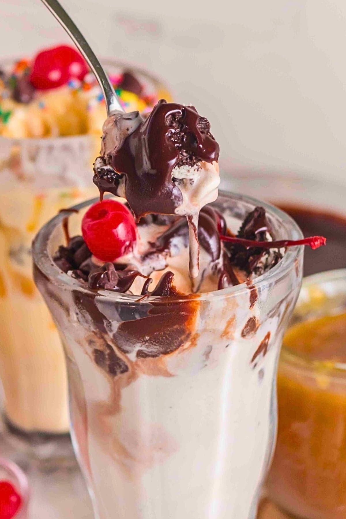 A hot fudge sundae with a cherry on top and a spoonful of ice cream lifted up.
