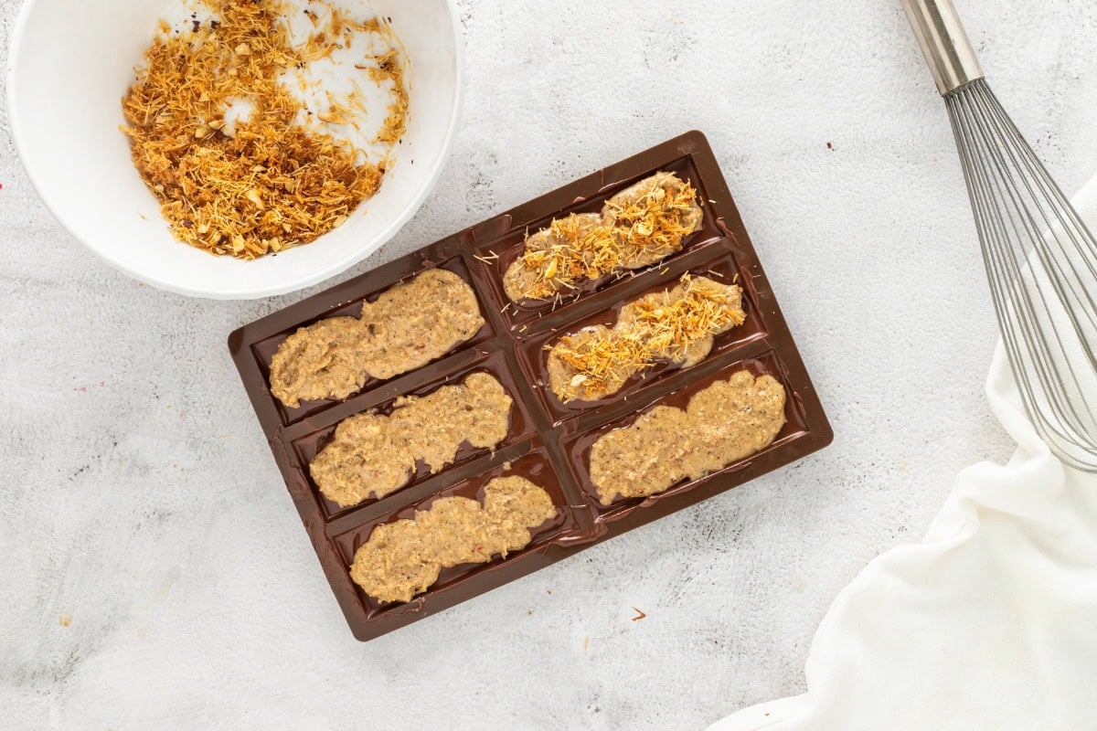 Chocolate bar mold with mixture, topped with shredded ingredients in a bowl.