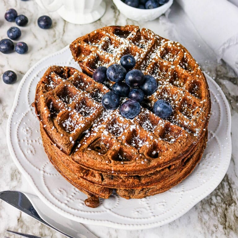 Stack of waffles topped with blueberries and powdered sugar on a white plate.