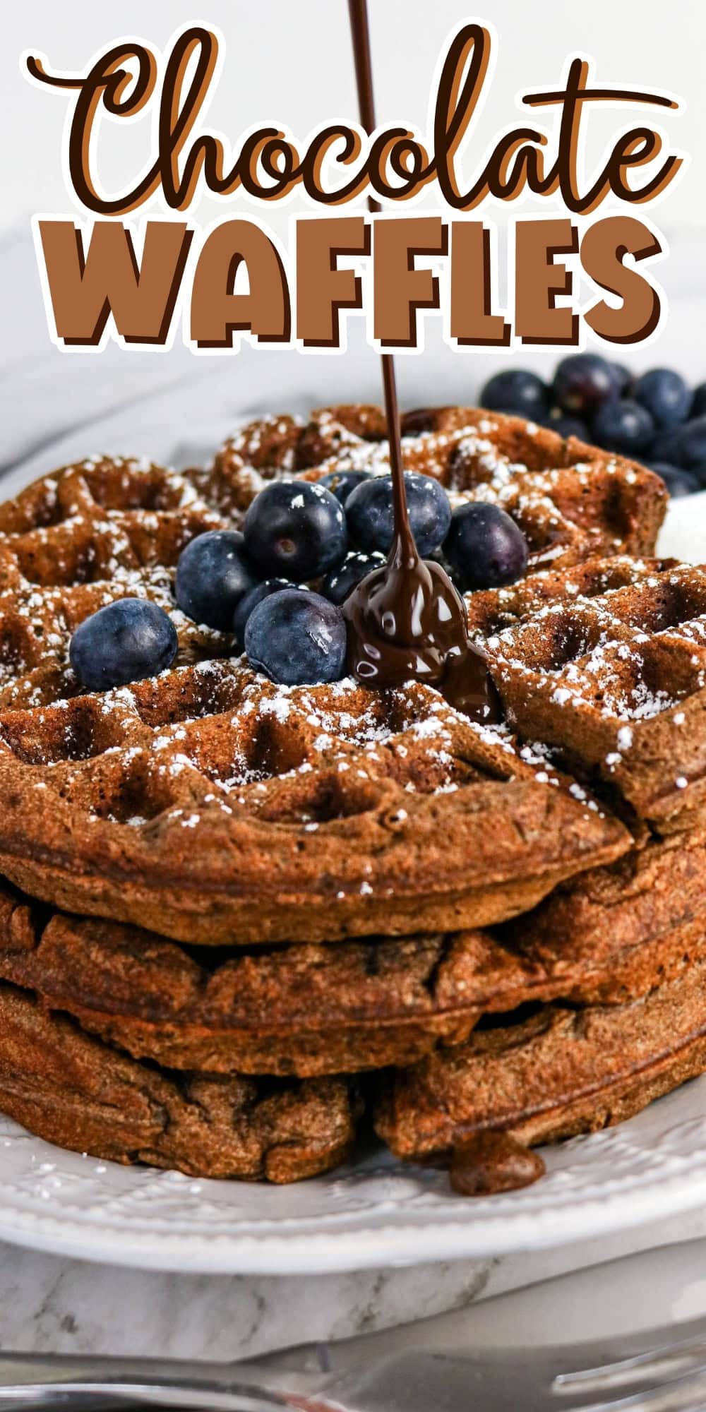 Chocolate waffles topped with blueberries, powdered sugar, and chocolate sauce.