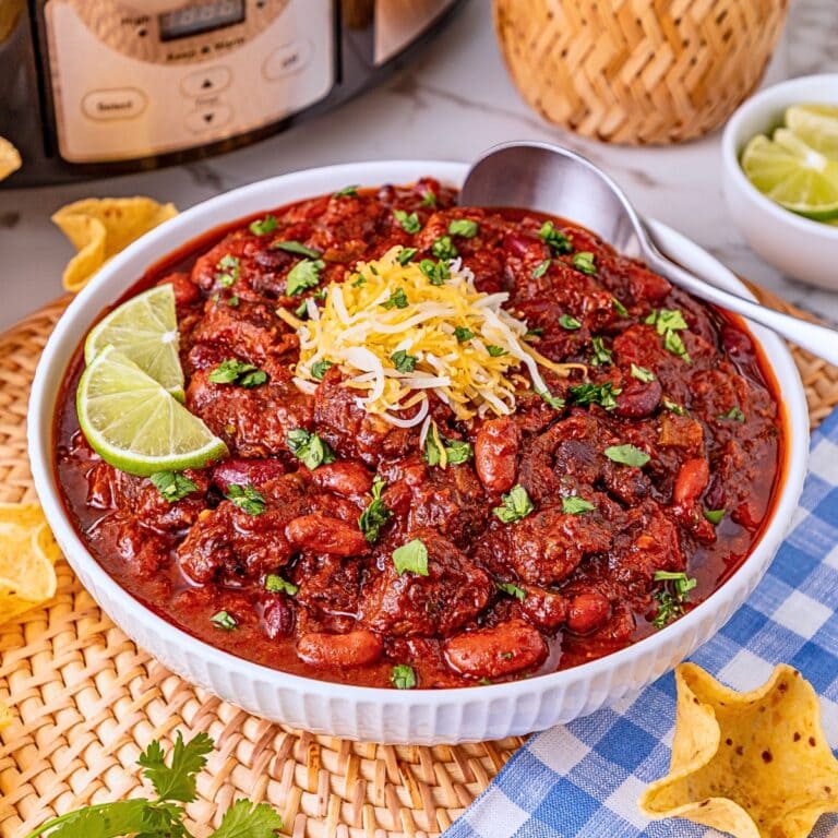 A bowl of chili topped with cheese, cilantro, and lime, with chips on the side.
