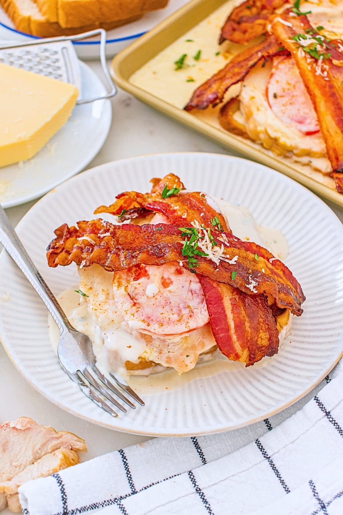 Open-faced sandwich with bacon, tomato, and creamy sauce on a white plate.