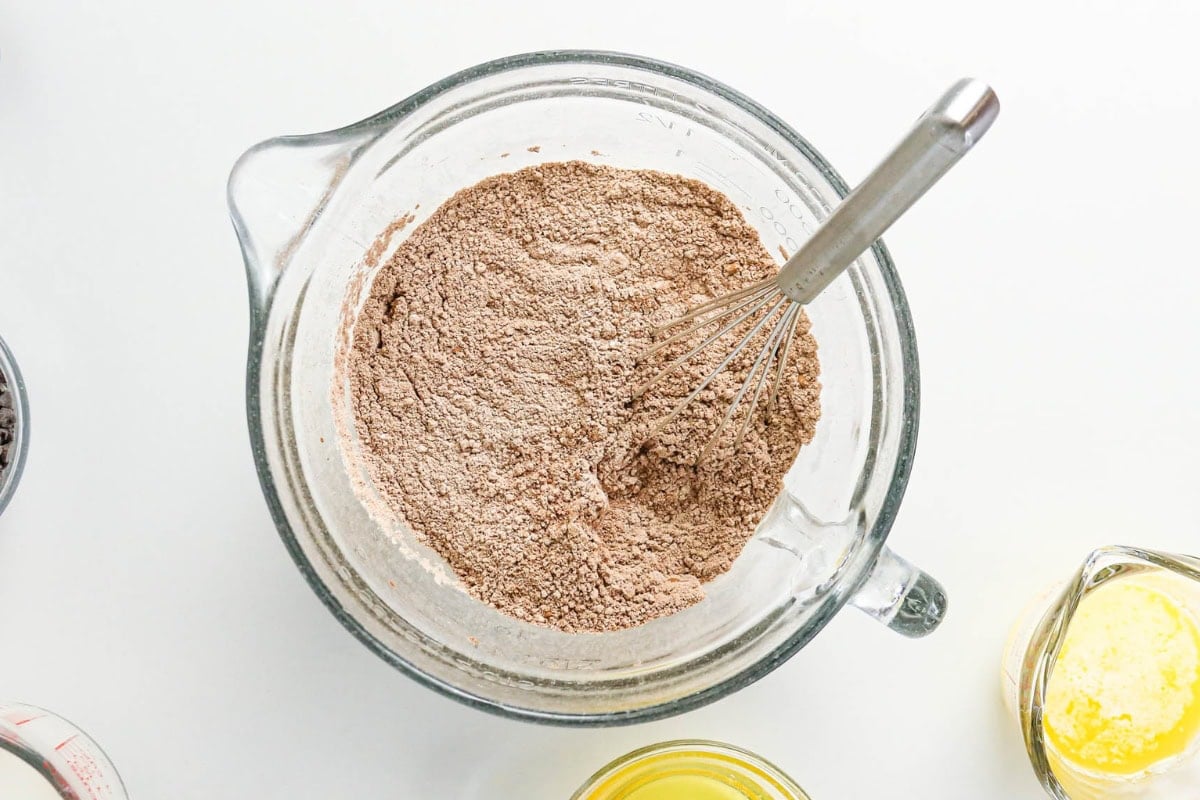 Bowl of cocoa powder mixture with a whisk on a white surface.