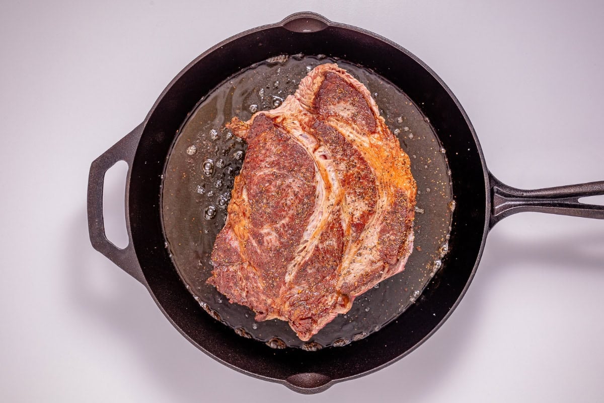 Seasoned steak cooking in a black cast iron skillet with oil.