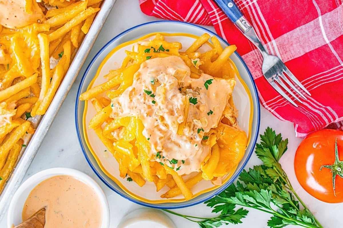 Plate of cheesy fries topped with creamy sauce, garnished with chopped parsley.