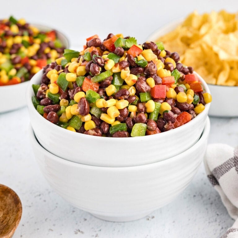 Bean, corn, and pepper salad in a white bowl with chips in the background.
