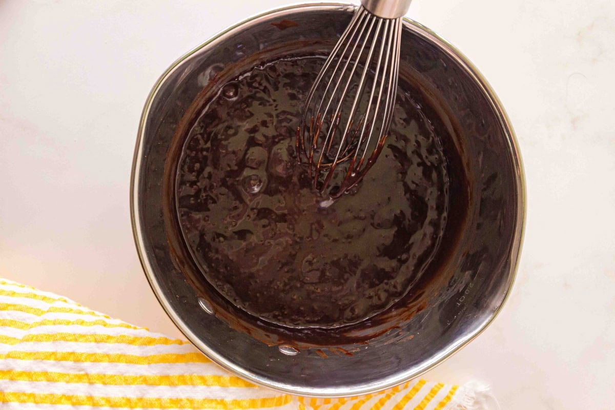 Metal whisk mixing chocolate batter in a metal bowl next to a yellow striped towel.