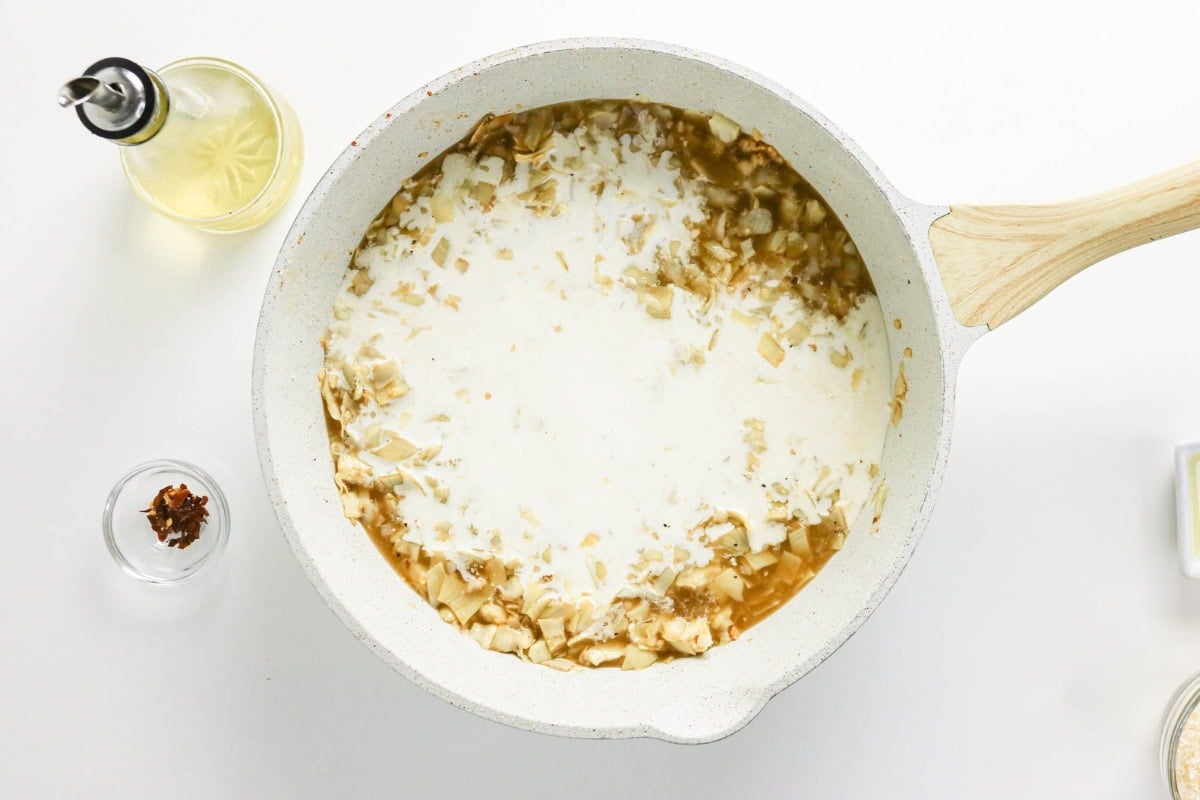 White skillet with creamy sauce and chopped onions on a white background.