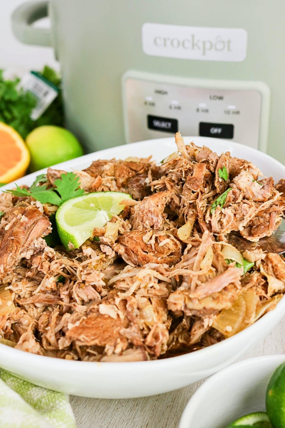Shredded pork with lime and cilantro in a bowl, slow cooker in background.