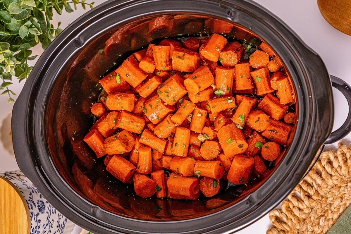 Chopped carrots with herbs in a black slow cooker on a table.